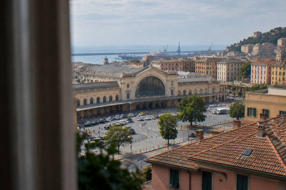 Hotel room window overlooking tiled rooftops toward the sea