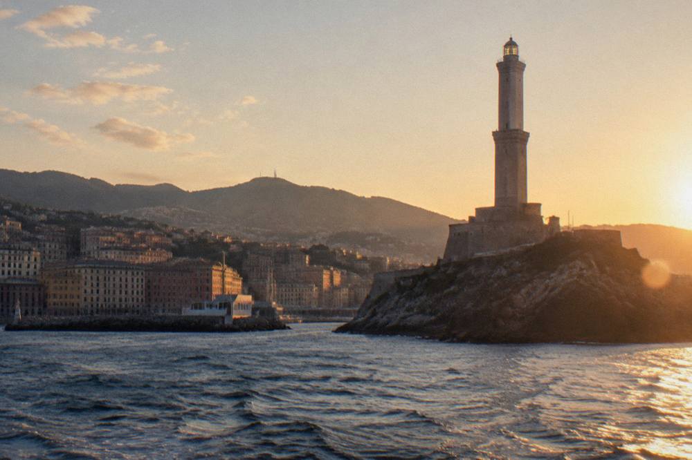 White lighthouse tower of the Lanterna seen from the water at dusk
