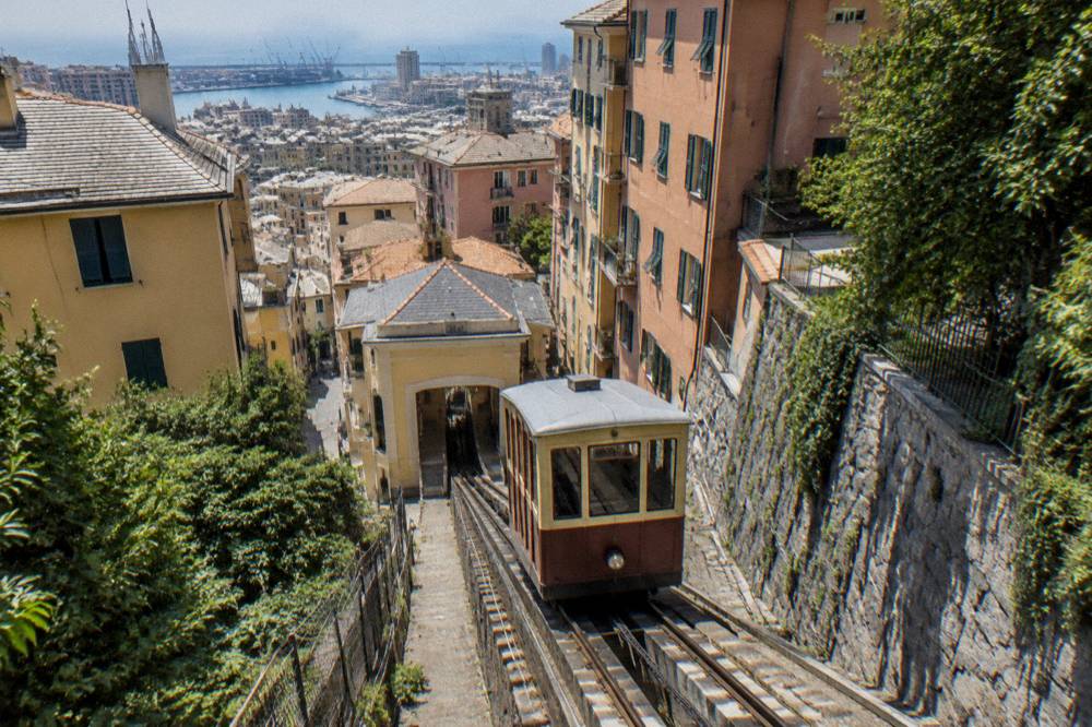 Funicular carriage climbing a steep rail track between buildings in Genoa