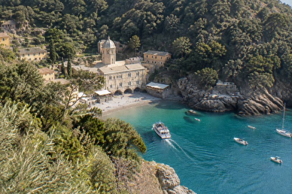 A small ferry approaching the sandy cove and abbey tower at San Fruttuoso