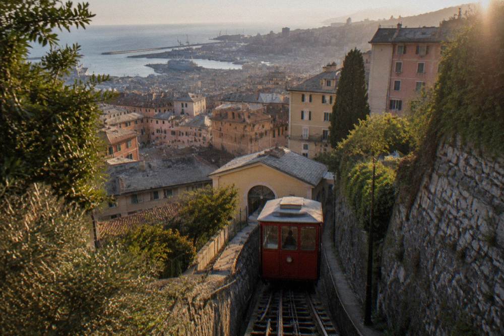 A red funicular car climbing the hillside above the rooftops of Genoa