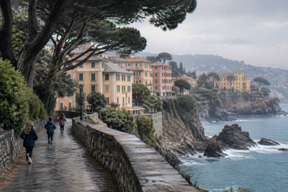 Children running along a seaside cliff path beside pine trees at Nervi
