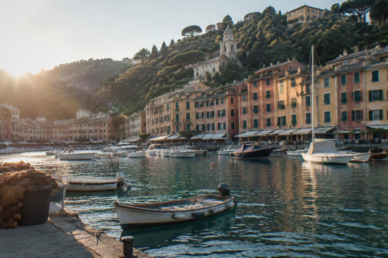 Pastel buildings rising above a small harbour on the Ligurian coast with fishing boats moored in clear water