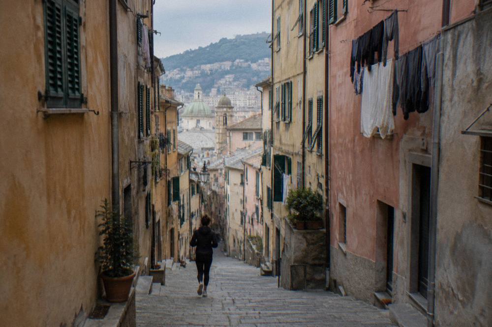 Narrow medieval lane in Genoa with tall painted buildings on both sides and laundry above