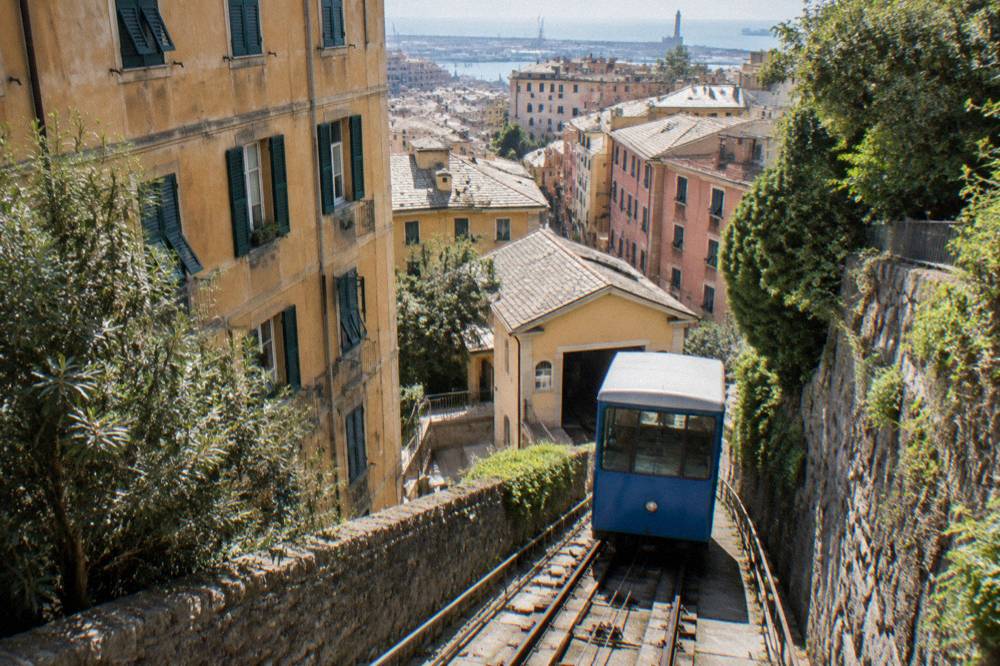 Blue funicular carriage climbing a steep track between old apartment buildings in Genoa