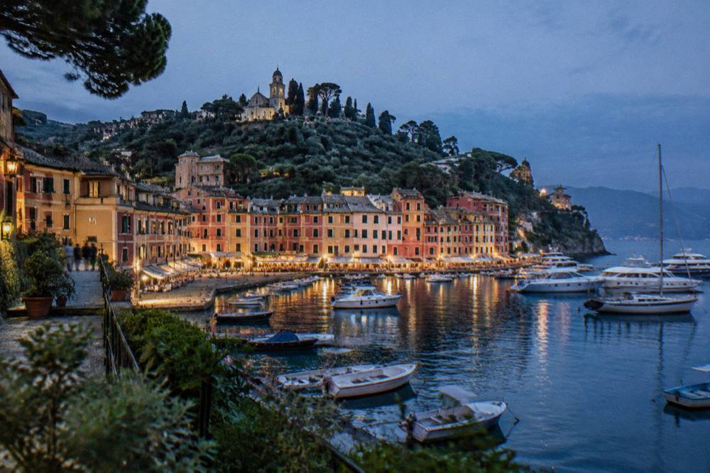 Evening view over a lit harbour with a panoramic lift tower and boats along the quays