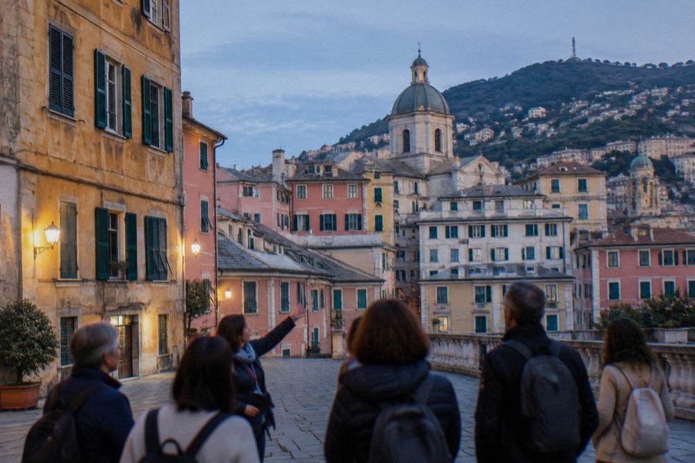 A small group of visitors listening to a guide in a square in Genoa