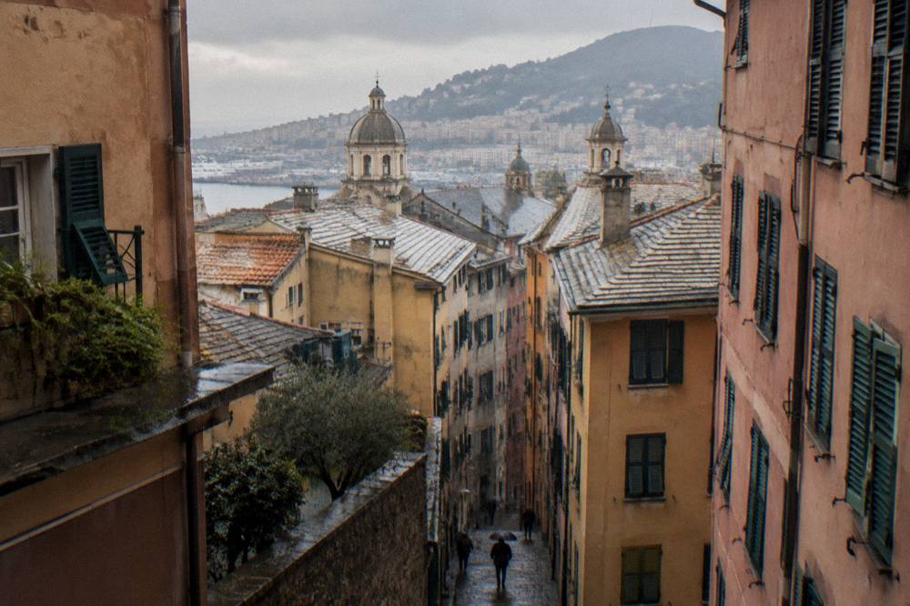 Tall shuttered buildings closing in over a narrow cobbled lane in Genoa