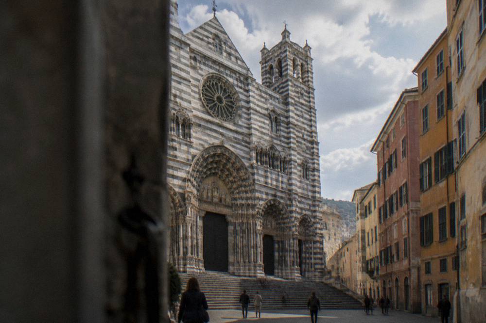 The striped facade of the Cathedral of San Lorenzo seen from a small square in Genoa