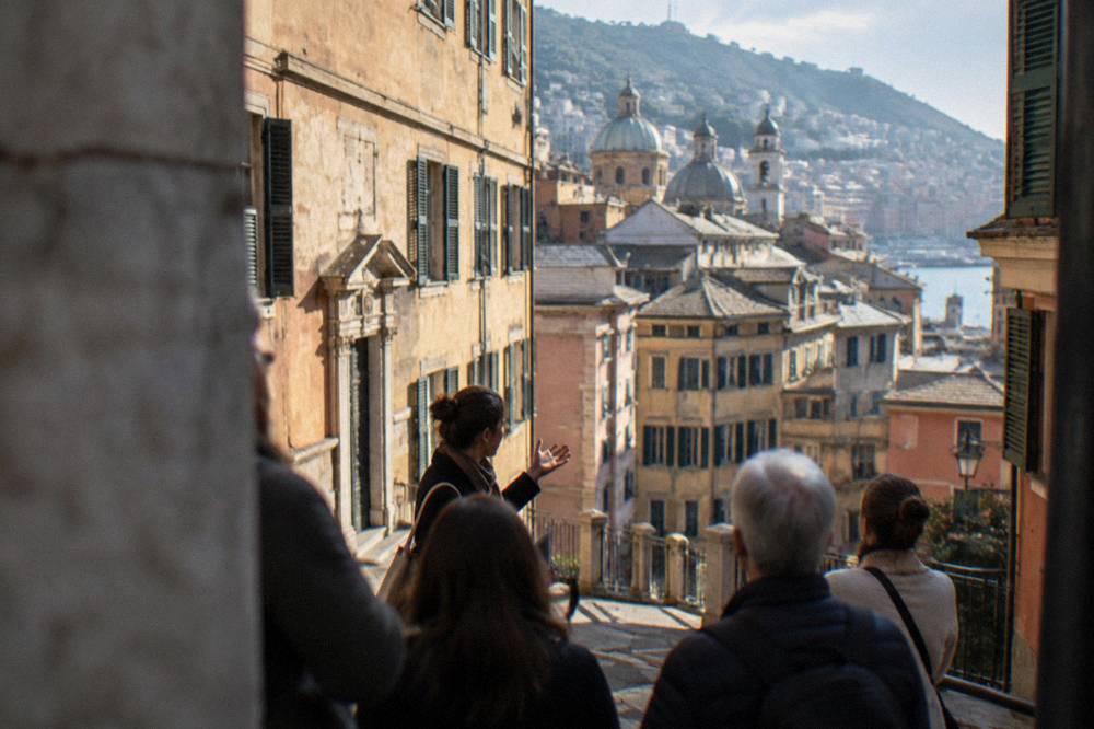 A guide speaking to a small group beside old palaces on a Genoa street